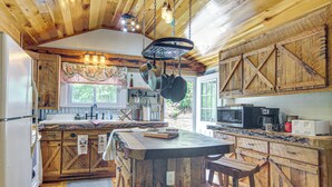 A rustic kitchen with wooden cabinets, a central island with stools, hanging pots, and a window providing natural light. - 20-acre Cabin w/ Pond: 6 Mi to River Arts District (Asheville)