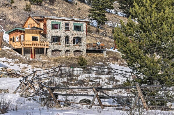 A rustic stone building with a wooden balcony, surrounded by snow and trees. - 'sasquatch Inn' Retreat Near Fishing & Hunting! (Wise River)