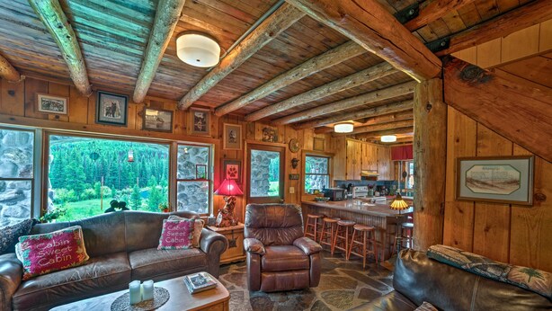 A rustic cabin interior with a stone floor, leather furniture, and a kitchen area visible through an open doorway. - 'sasquatch Inn' Retreat Near Fishing & Hunting! (Wise River)