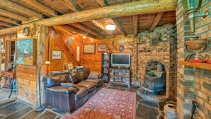 A rustic cabin interior with a leather sofa, stone flooring, a brick fireplace, and a television. - 'sasquatch Inn' Retreat Near Fishing & Hunting! (Wise River)