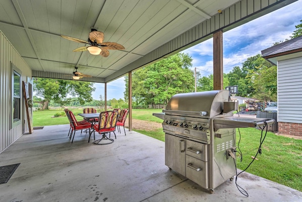An outdoor patio with a grill, chairs, and a ceiling fan.