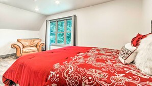 Een slaapkamer met een groot bed, een raam met gordijnen, een leren fauteuil en een zacht, bekleed kussen.