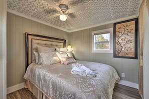 A bedroom with a tufted headboard, a bed with patterned bedding, a ceiling fan, and a wall-mounted artwork.