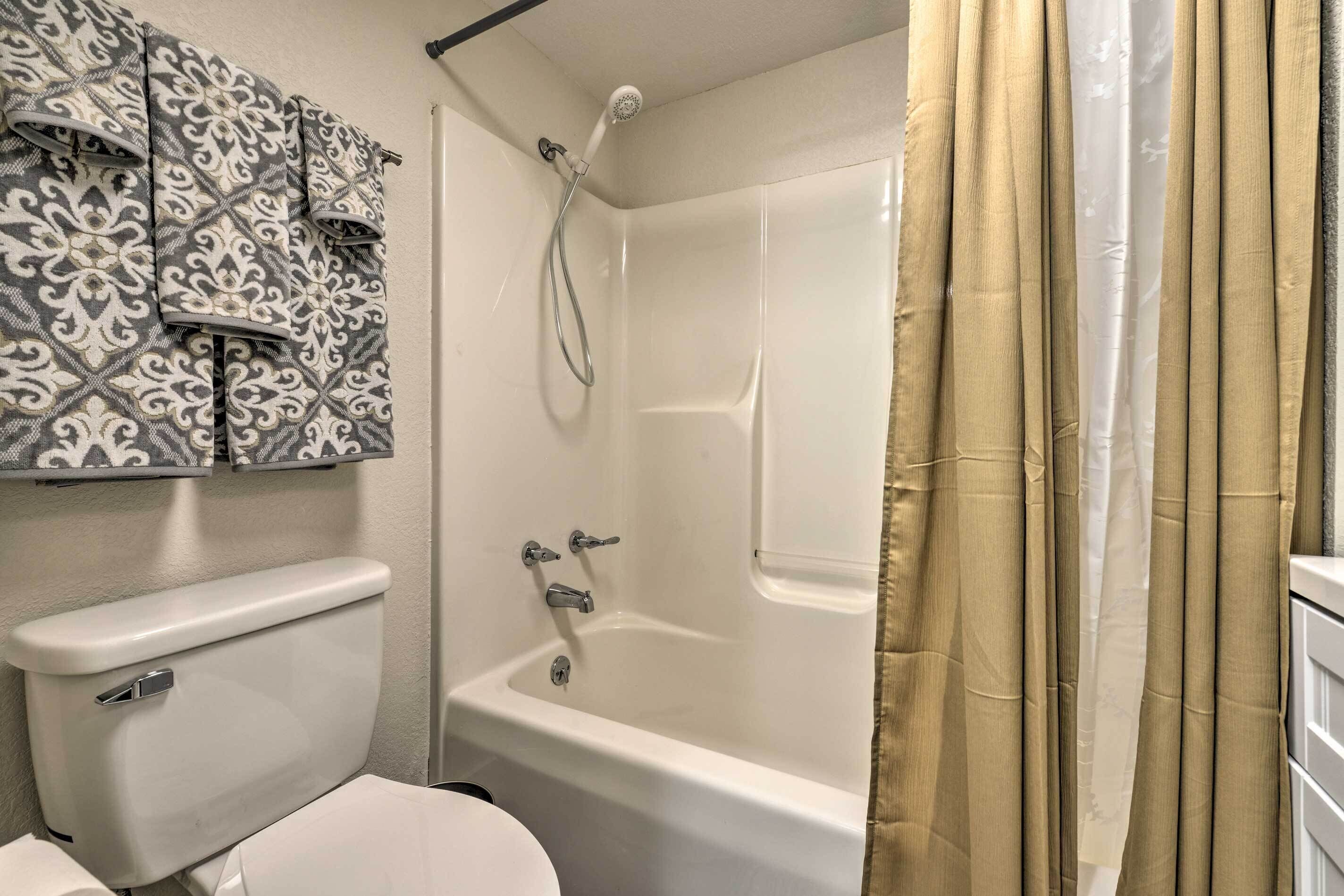 A bathroom with a toilet, a shower with a curtain, and patterned tiles on the wall.