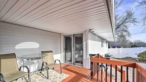 A covered deck with a glass table and chairs, a sliding glass door, and a wooden railing.