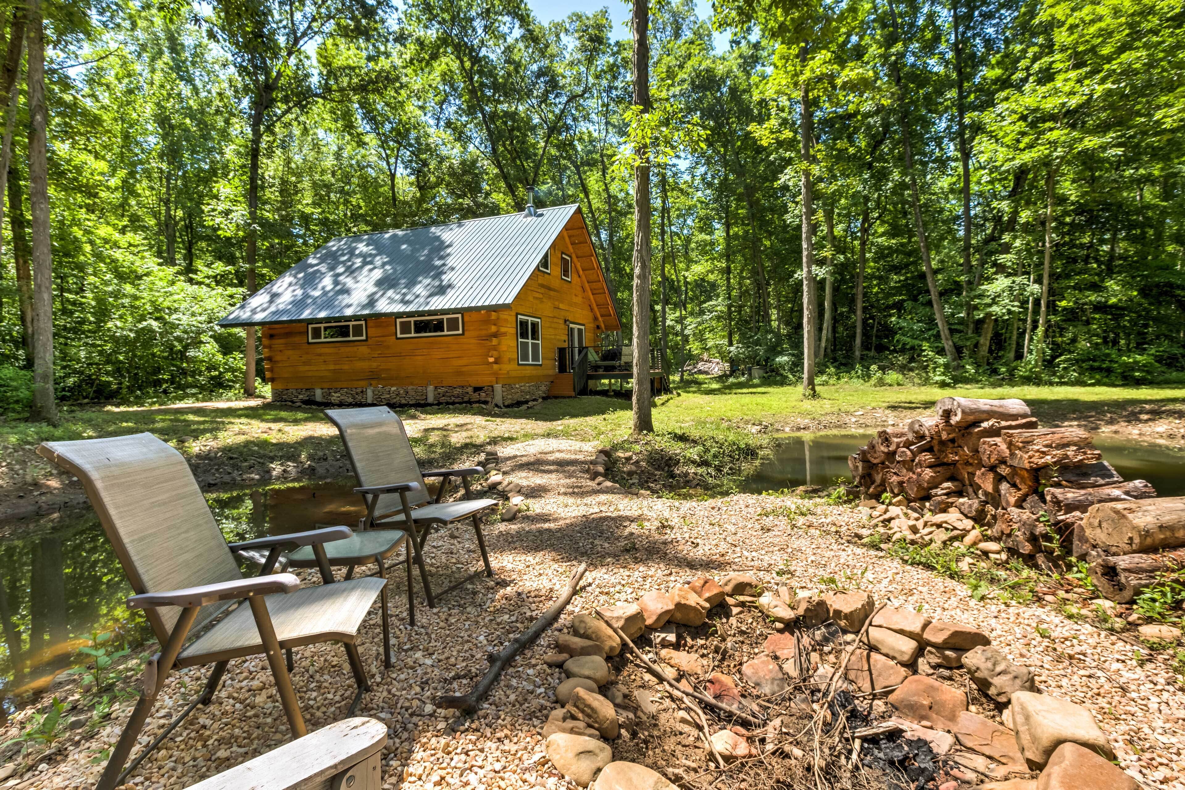 A cabin with a stone foundation, a metal roof, and a fire pit in the foreground.