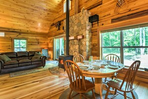 Een gezellig cabin interieur met een stenen openhaard, houten meubels en grote ramen met uitzicht op het bos.