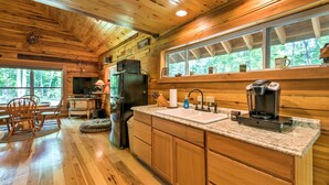 Cocina de cabaña de madera con una isla grande, armarios de madera, un refrigerador, una cafetera y un ventanal con vistas al bosque.