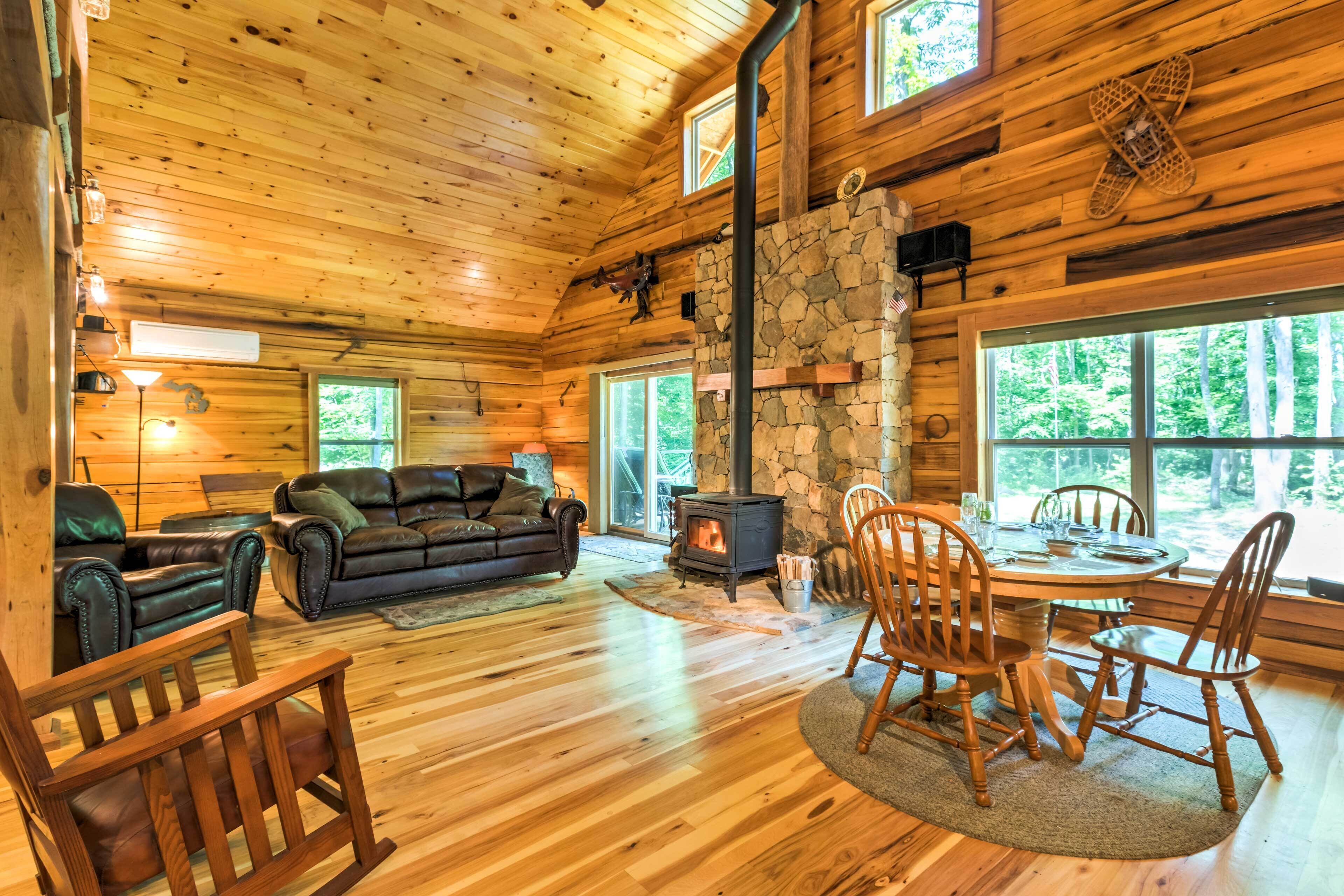 A cozy cabin interior with a stone fireplace, wooden walls, leather sofas, and a dining area.