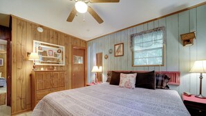 Un dormitorio con un armario de madera, una cama con ropa de cama estampada, un ventilador de techo y una ventana con persianas.