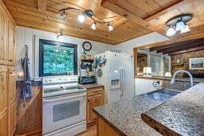 A kitchen with wooden cabinets, a built-in oven, a refrigerator, and granite countertops. - Sweet Birch' Bryson City Cottage w/ Views (Bryson City)