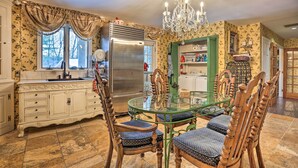 A dining area with a glass table, wooden chairs, a chandelier, and a kitchen in the background.