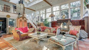 A spacious room with a high ceiling, large windows, and a staircase leading to an upper level.