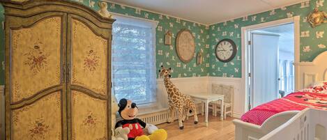 Una stanza con un armadio in stile vintage, un grande peluche a forma di giraffa, una panca bianca e un letto con copriletto a pois rossi.