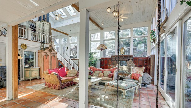 A spacious living room with a high ceiling, large windows, and a variety of seating options.