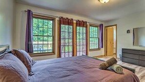 Une chambre à coucher avec un grand lit, deux fenêtres avec des rideaux, une commode et une porte donnant sur une autre pièce.