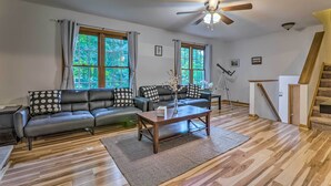 Un salon moderne avec un canapé d’angle, une table basse en bois et de grandes fenêtres agrémentées de rideaux.