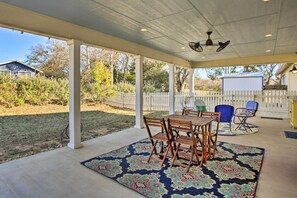 A covered patio with a table and chairs, a white picket fence, and a view of a backyard.