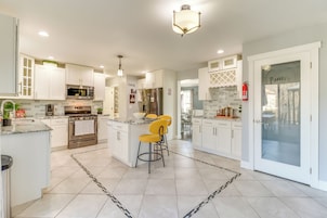 Una cocina moderna con armarios blancos, un horno de acero inoxidable y una isla central con taburetes amarillos.
