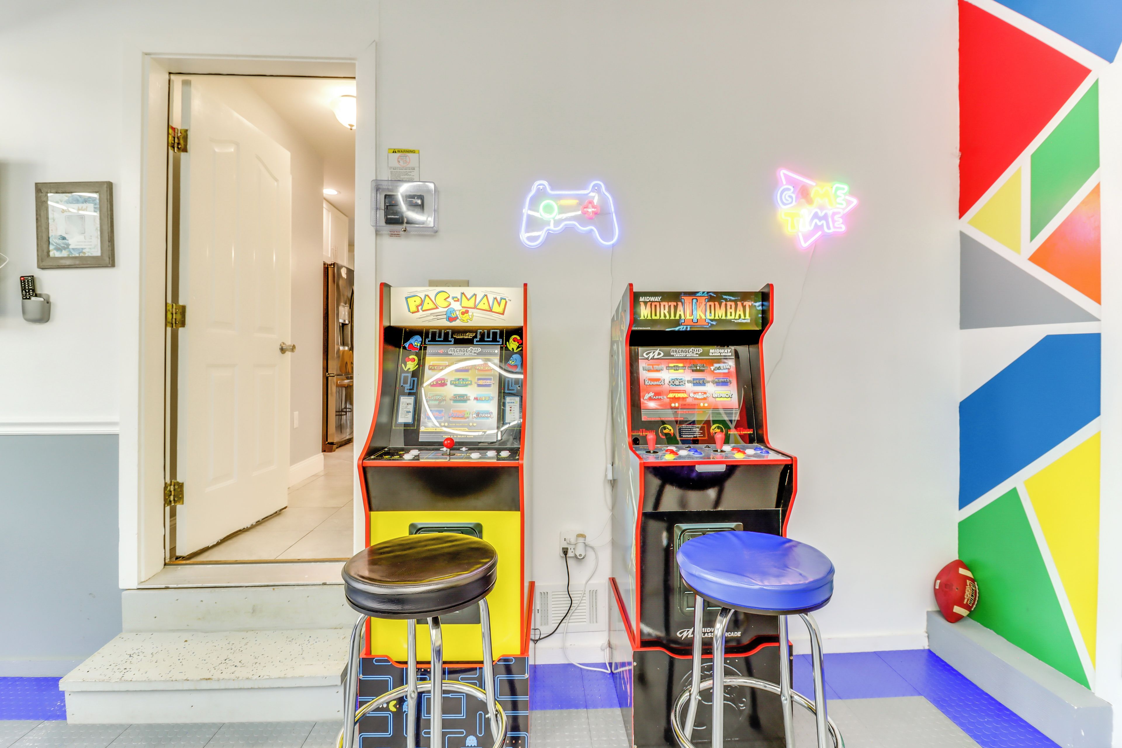 A room with two arcade machines, a neon sign, and a colorful geometric wall.