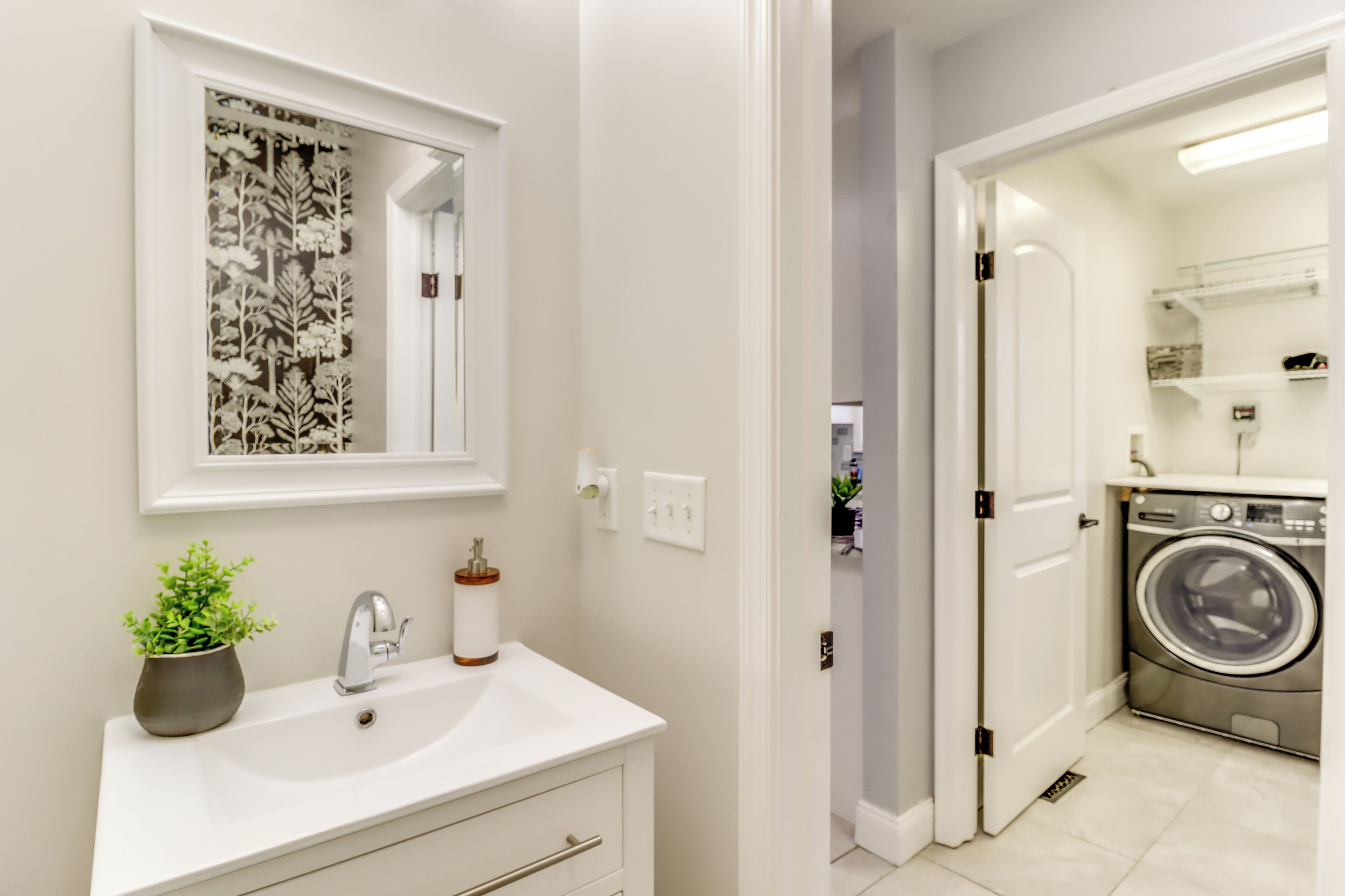 A modern bathroom with a white sink, mirror, and potted plant.