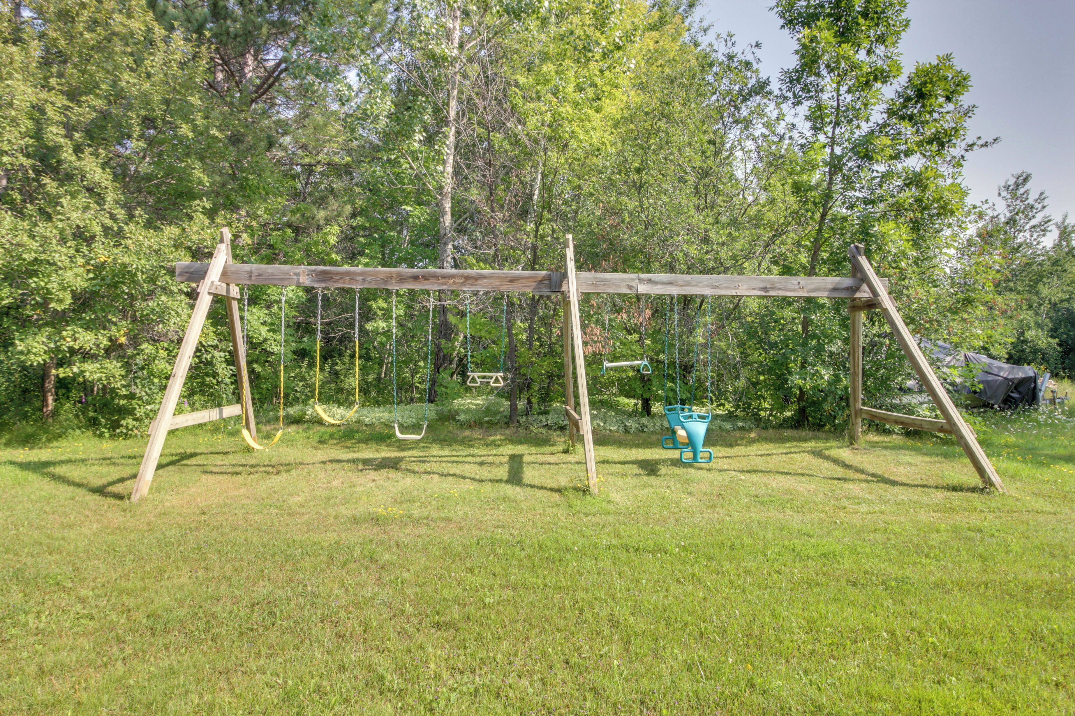 A wooden swing set in a grassy area with trees in the background.