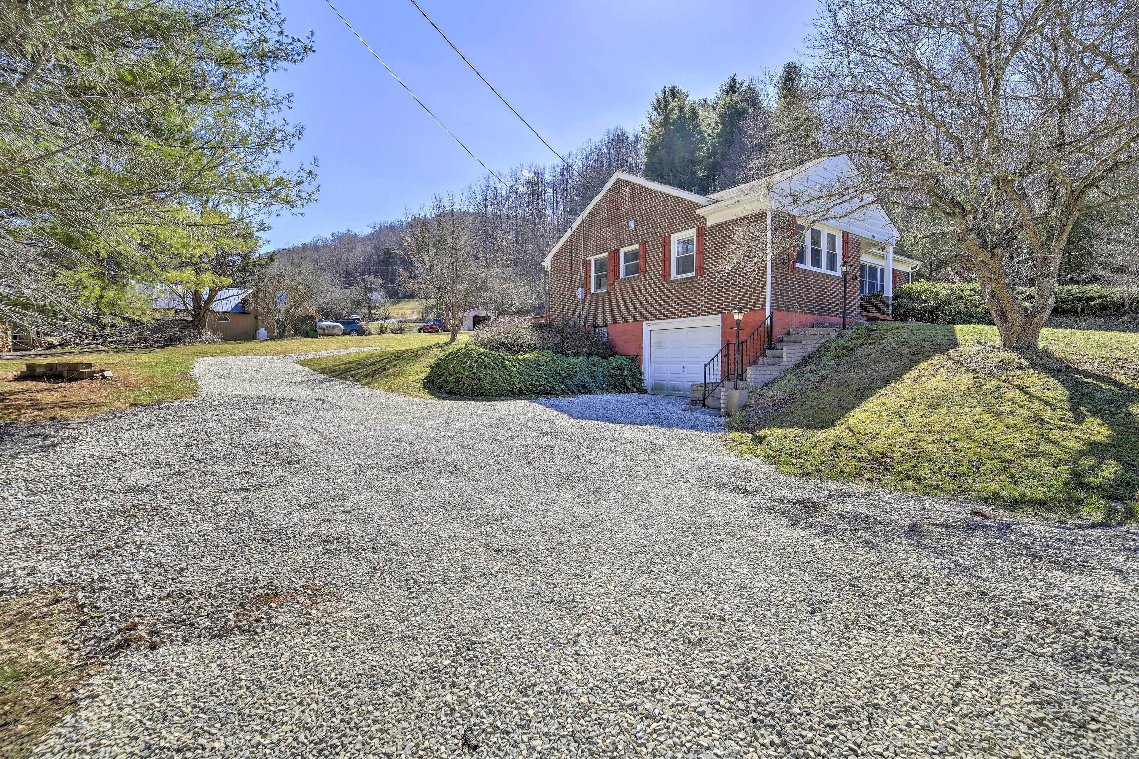 A two-story brick house with a garage, surrounded by a gravel driveway and a grassy area.