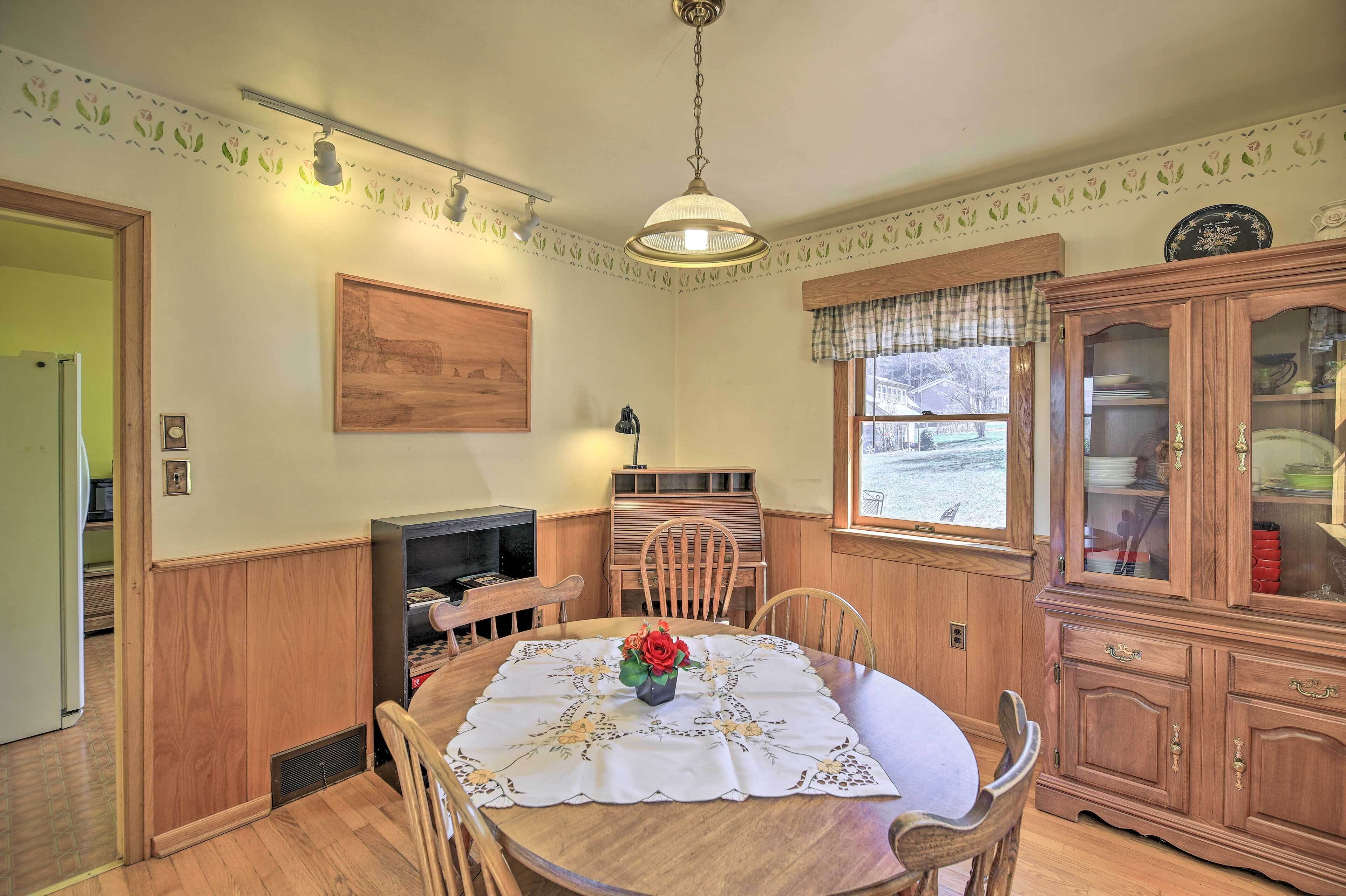A dining room with a round table, chairs, a wooden cabinet, and a window with a view.