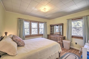 A bedroom with a large bed, a dresser, a mirror, and two windows with curtains. - Quaint Creekside Home w/ Spacious Deck & Yard (Atkins)