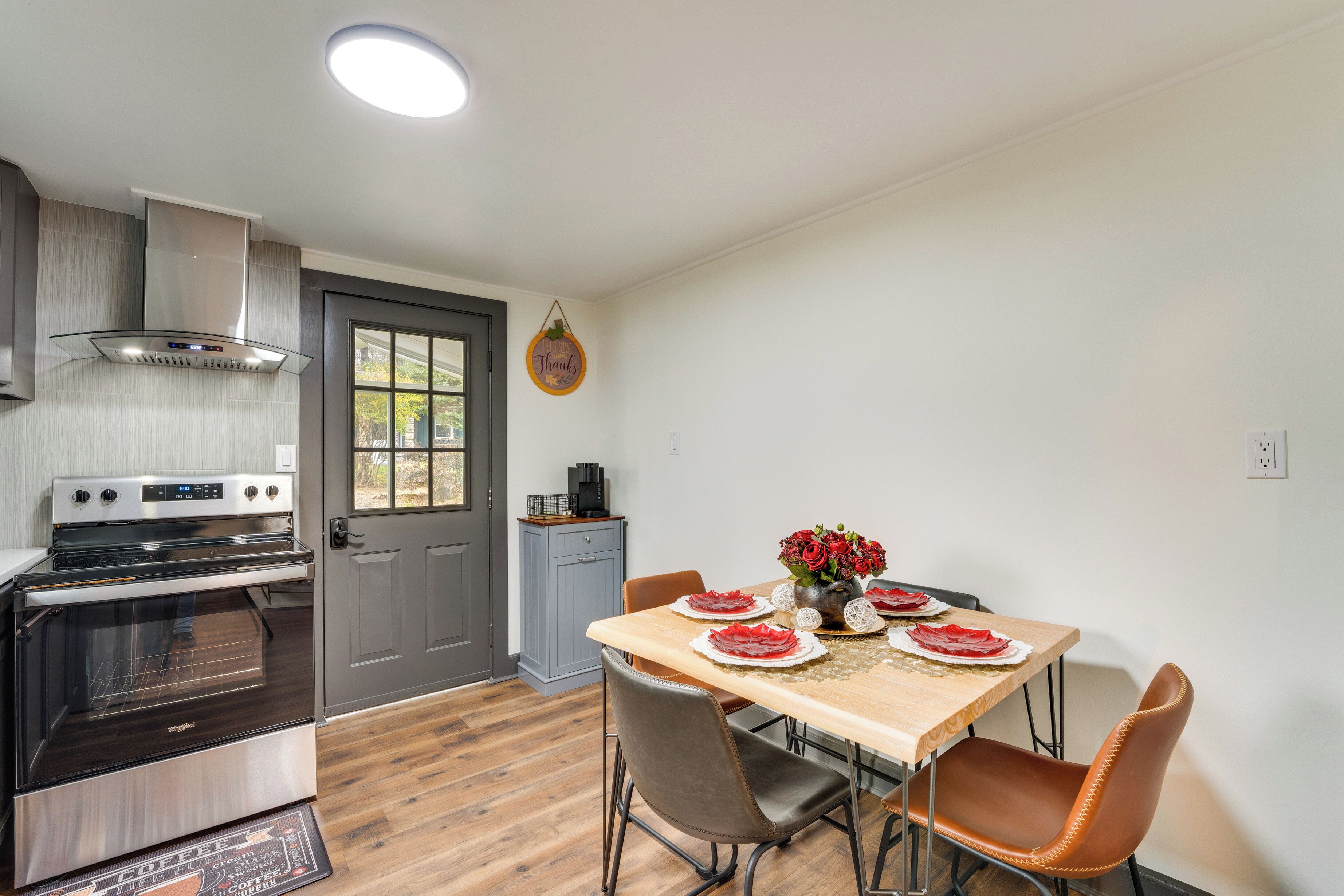 Una cocina moderna con horno empotrado, estufa a gas y extractor de acero inoxidable. Hay una mesa de comedor con sillas y un jarrón con flores.