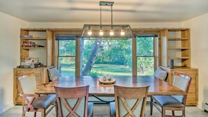 A dining area with a large wooden table, four chairs, and a chandelier. There are bookshelves on either side of the table and a window with a view of greenery outside. - 'moose Park Lodge' Charming Walden Retreat! (Walden)