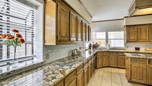 A kitchen with wooden cabinets, granite countertops, and a window with blinds. - Spacious Houston Getaway ~ 23 Mi to Downtown! (Houston)
