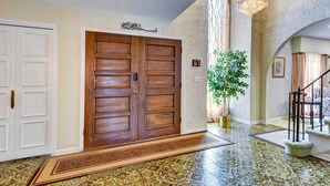 A foyer with a wooden double door, a potted plant, a patterned rug, and a staircase with a railing. - Spacious Buffalo Brick Home w/ Backyard! (Buffalo)