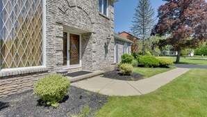 A stone house with a front door, a small front yard with a pathway, and a tree with red leaves. - Spacious Buffalo Brick Home w/ Backyard! (Buffalo)
