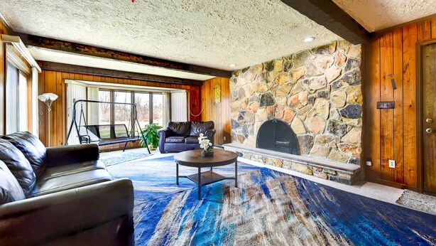 A living room with a stone fireplace, leather sofa, and a large window. - Spacious Buffalo Brick Home w/ Backyard! (Buffalo)