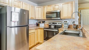 A modern kitchen with stainless steel appliances, wooden cabinets, granite countertops, and a built-in oven. - Condo Near Winter Park Resort + Steps From Shuttle (Fraser)