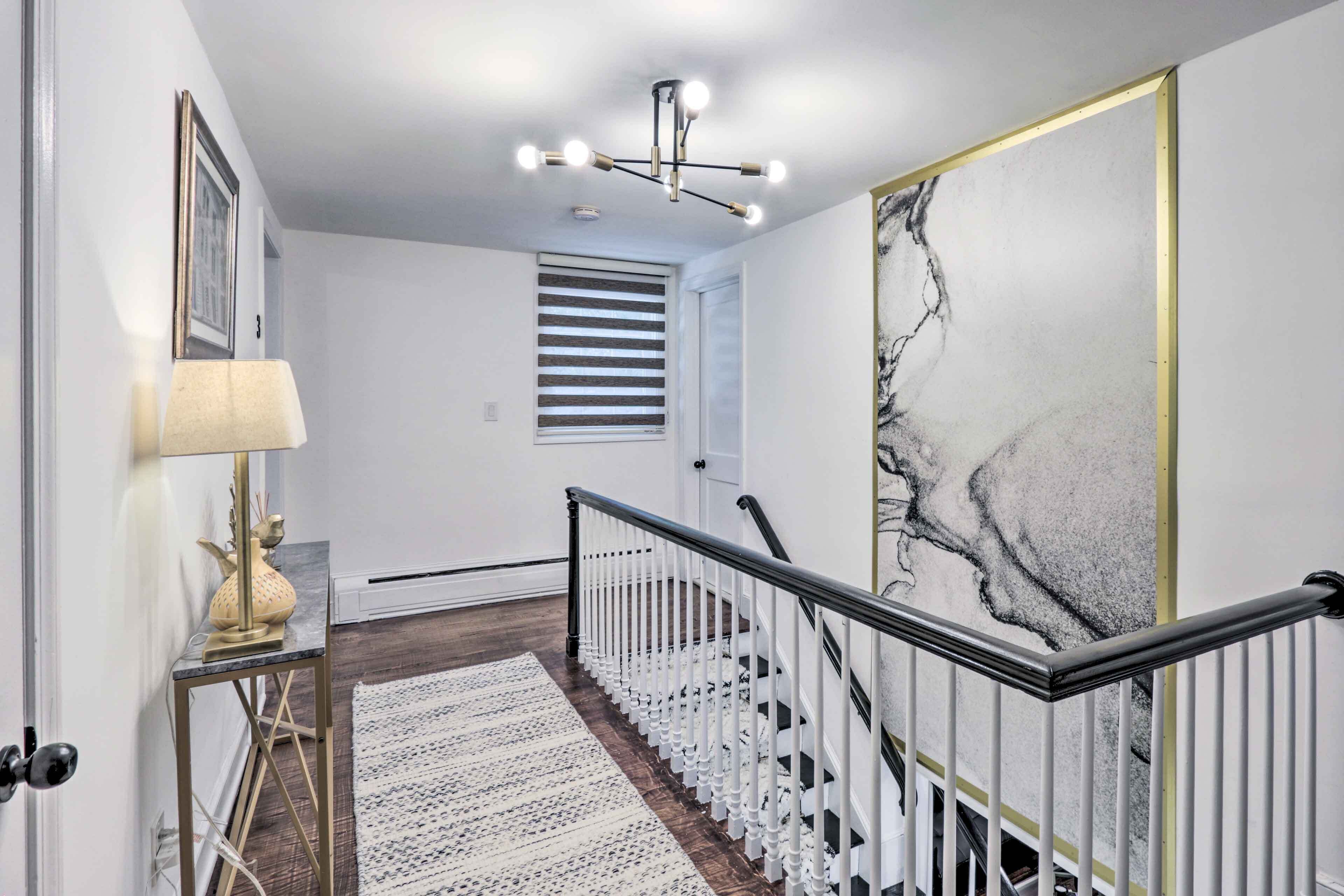 A staircase with white railings and a black handrail, leading to a room with a white door and a framed picture on the wall.
