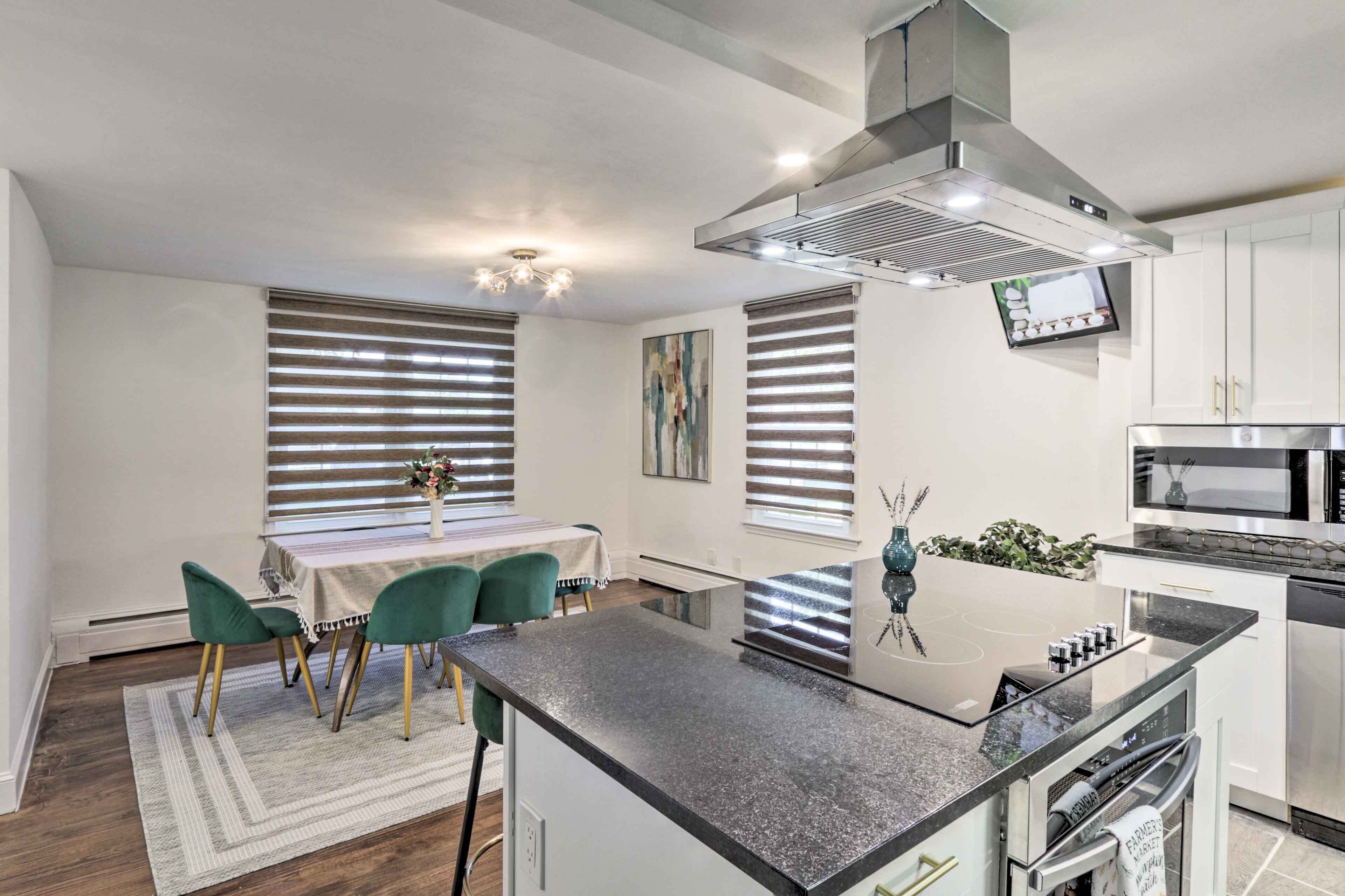 Een moderne keuken met een centraal eiland, roestvrijstalen apparatuur en een eethoek met een tafel en stoelen.