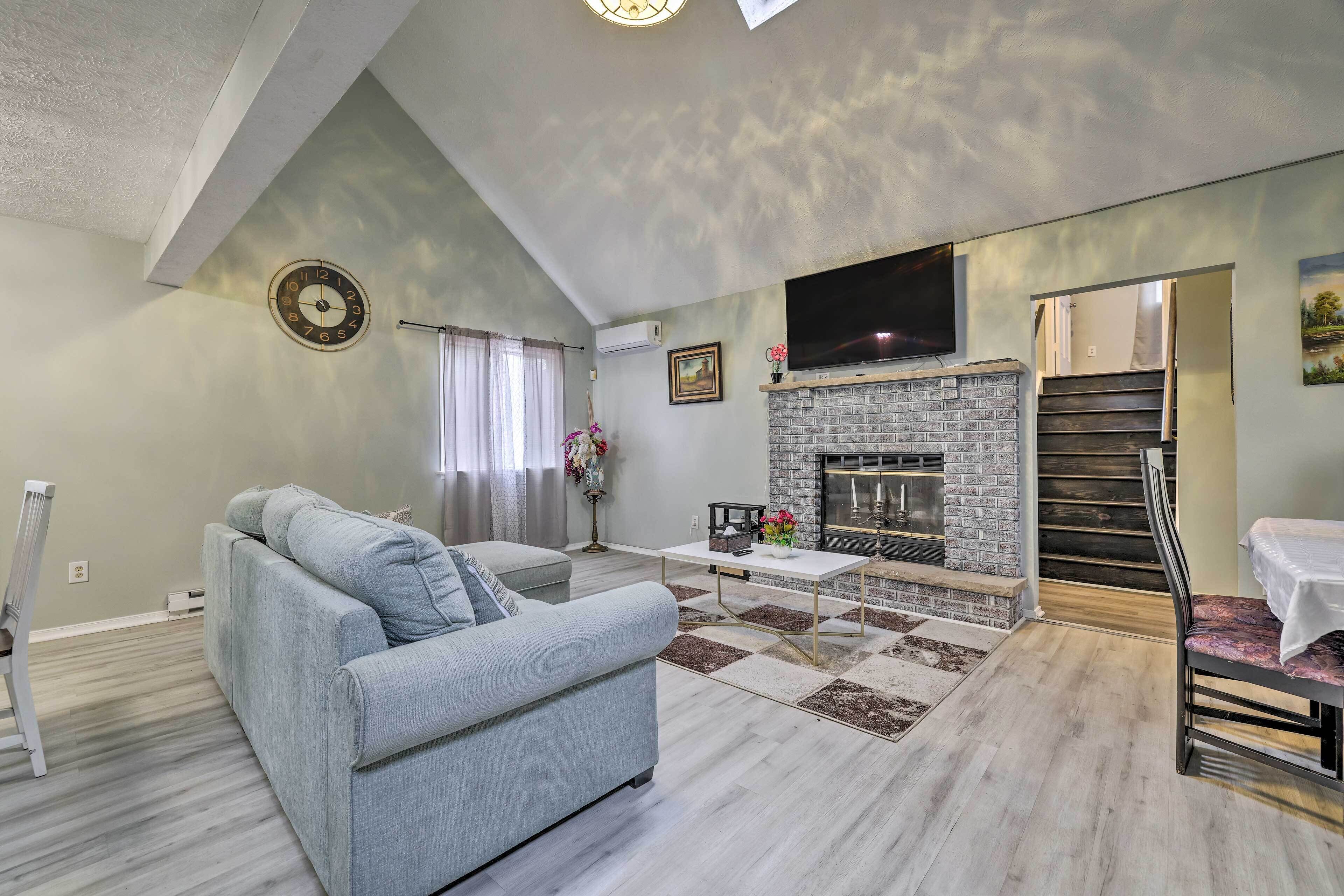 Ein modernes Wohnzimmer mit einem grauen Sofa, einem Kamin, einem Flachbildfernseher und einer Treppe, die zu einer weiteren Ebene führt.