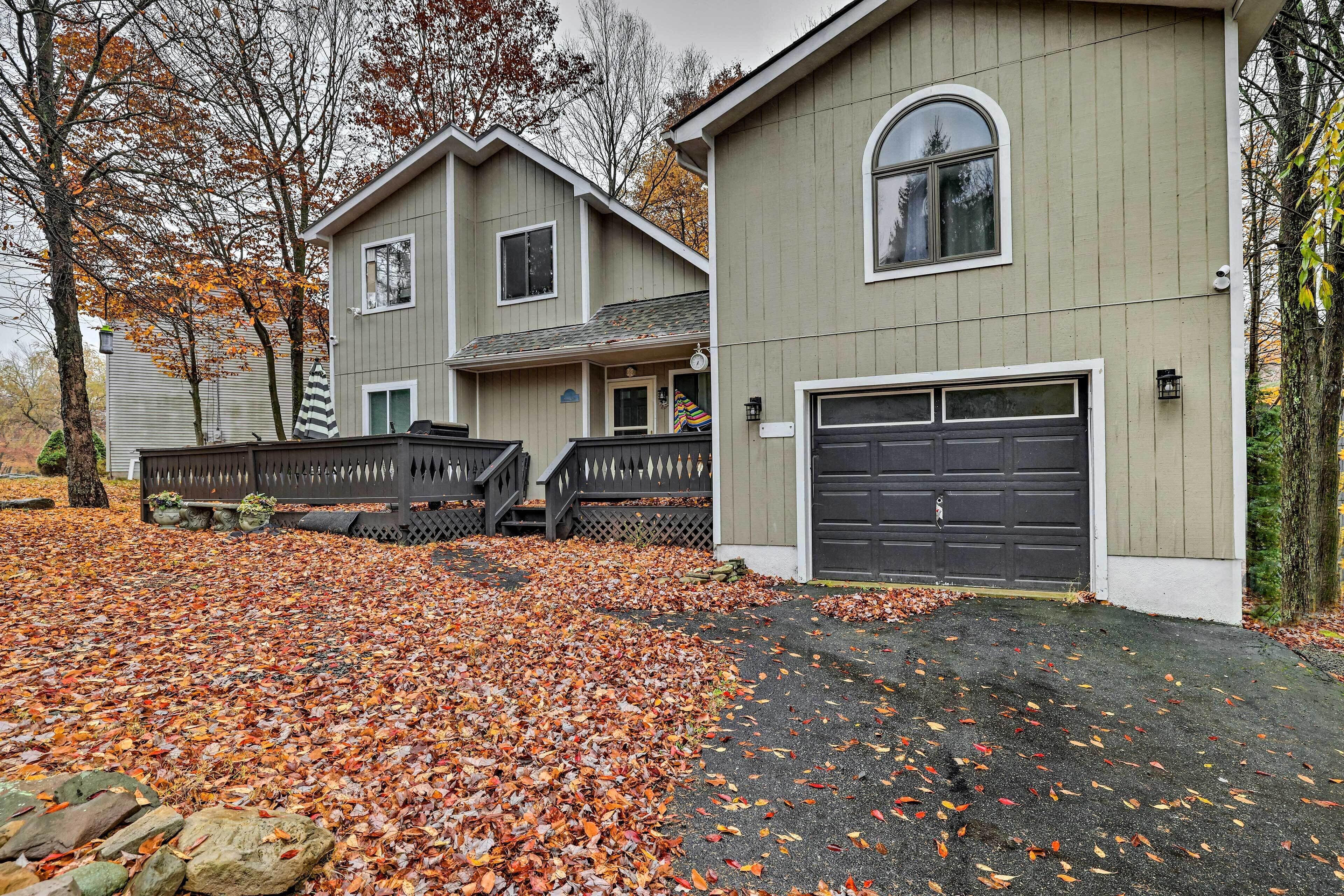 A two-story house with a garage, a front porch, and a driveway covered with fallen leaves.