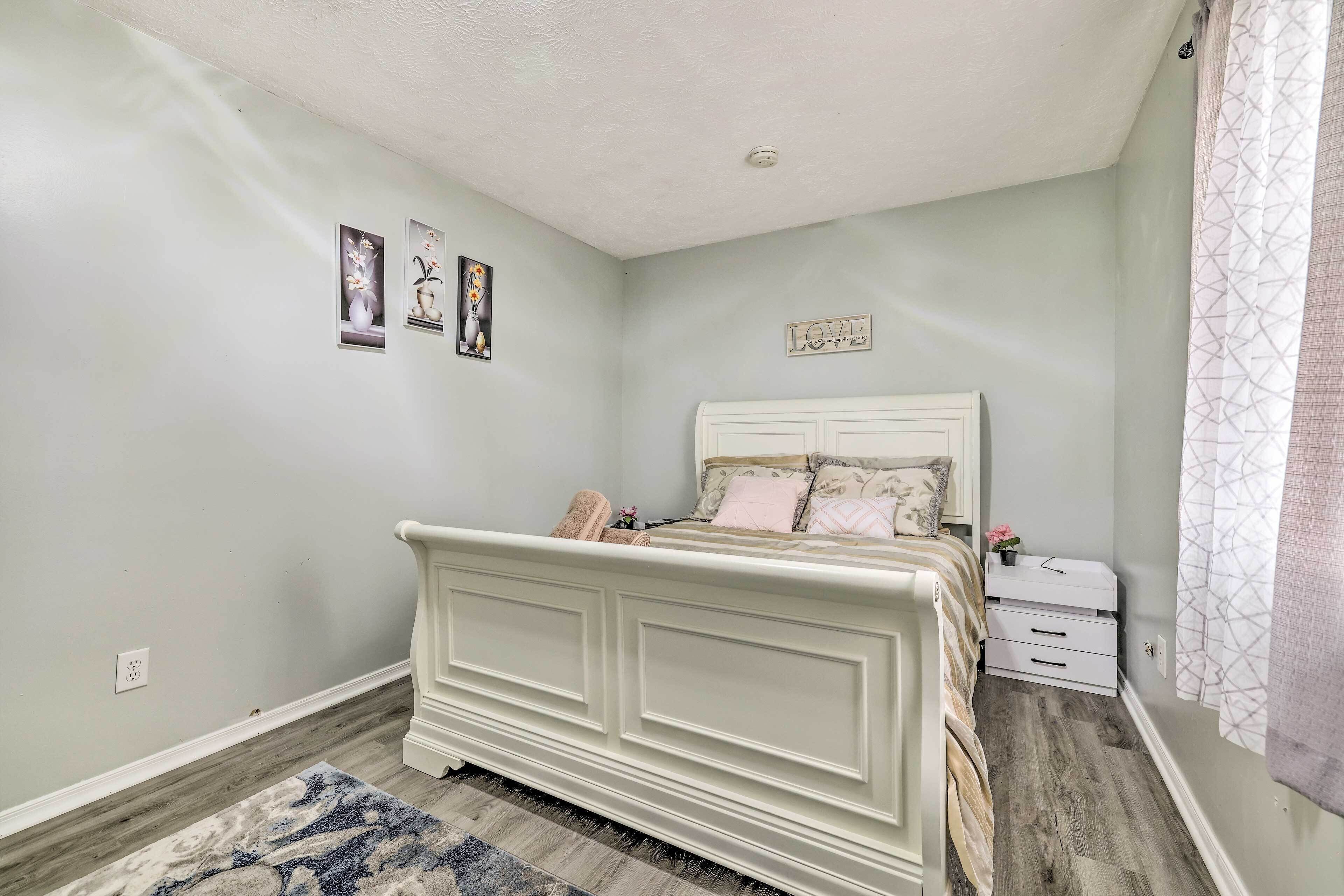 A bedroom with a white bed, a nightstand, a dresser, and a rug.