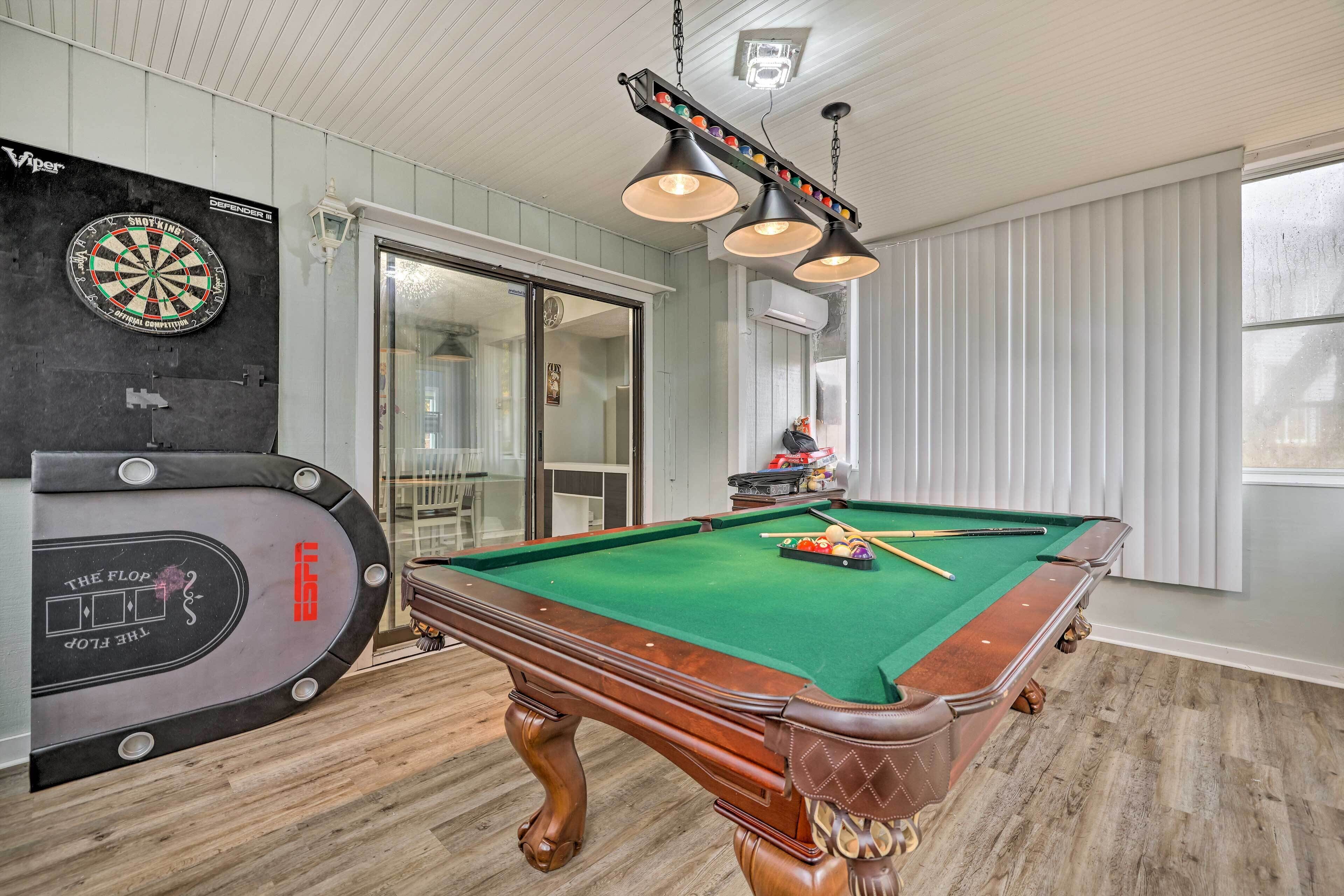 Une table de billard avec une queue de billard et des billes, un jeu de fléchettes et une table de billard recouverte de cuir.