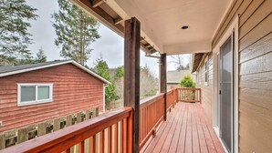 A wooden deck with a railing, a covered porch, and a view of a red building and trees. - Pet-friendly PNW Home, 1 Mi to Rockaway Beach (Rockaway Beach)