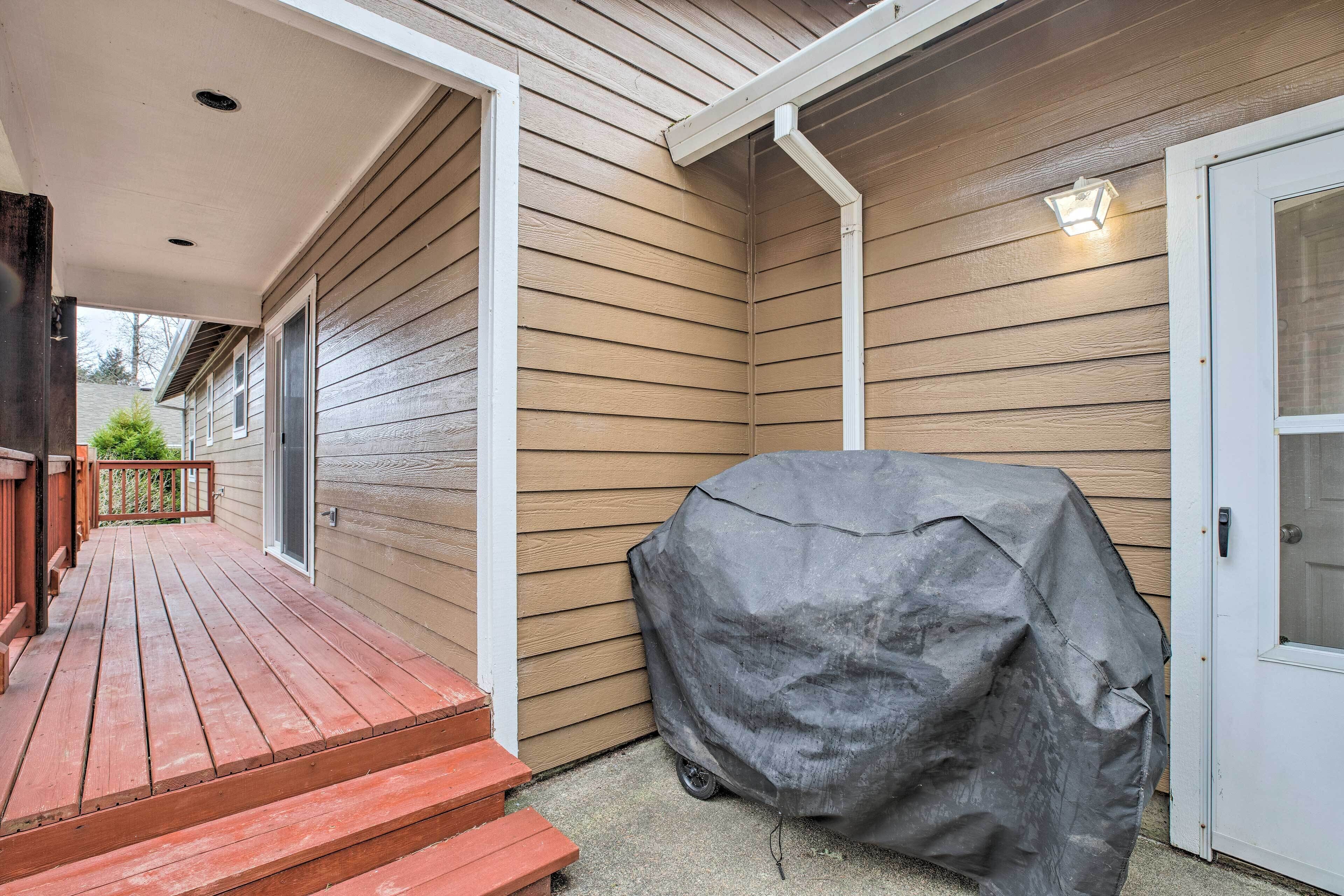 A wooden deck with a covered grill, a white door, and a light fixture on the wall.