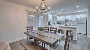 A modern kitchen with white cabinets, a central island, and a dining area with a wooden table and chairs. - Pet-friendly PNW Home, 1 Mi to Rockaway Beach (Rockaway Beach)