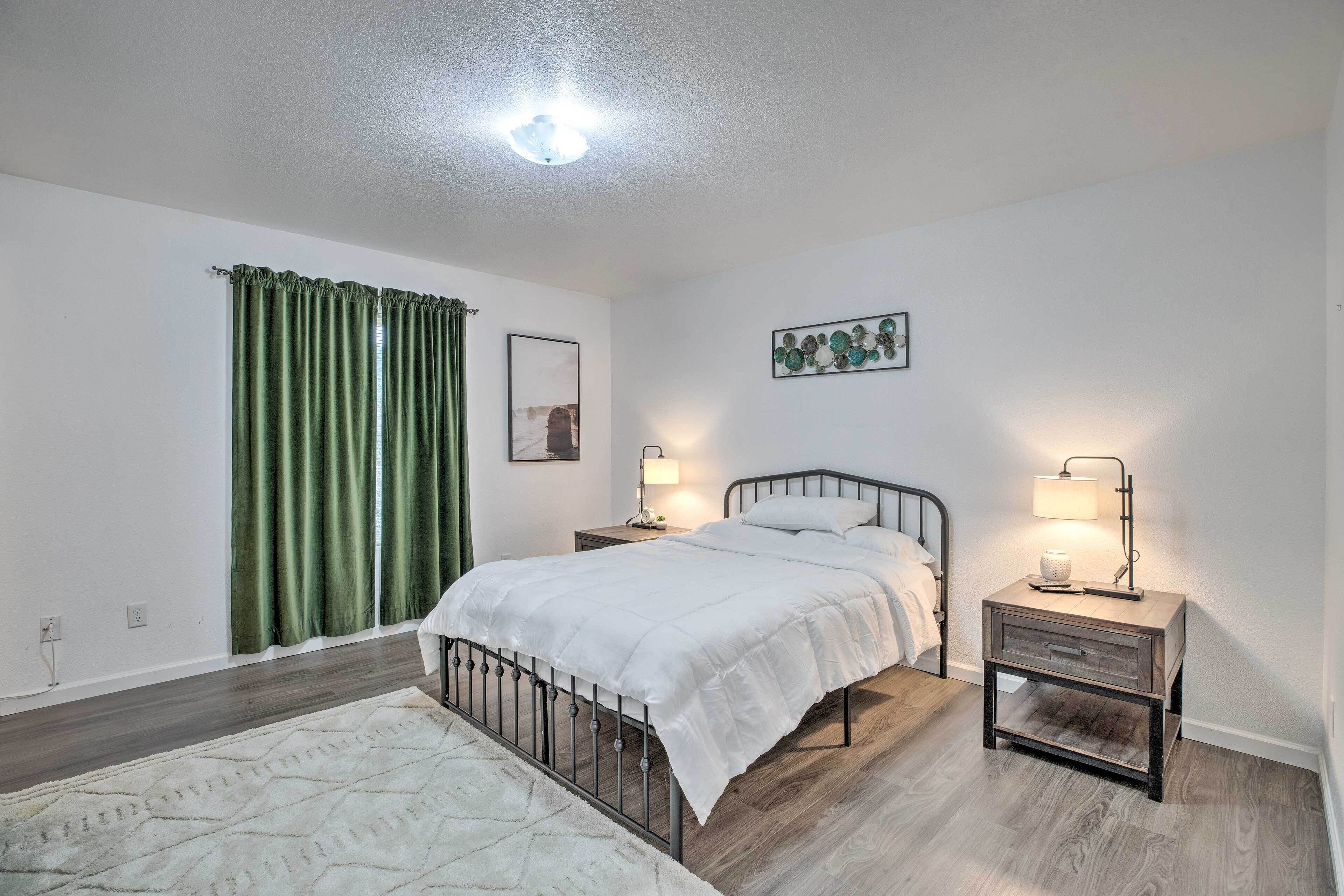 A bedroom with a bed, two bedside tables with lamps, a green curtain, a framed picture, and a light fixture on the ceiling.