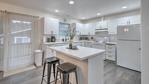 A modern kitchen with white cabinets, a central island with stools, and a refrigerator. - Pet-friendly PNW Home, 1 Mi to Rockaway Beach (Rockaway Beach)