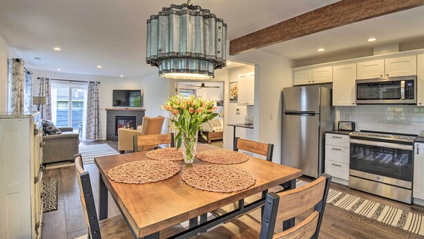 A modern kitchen with stainless steel appliances, a wooden dining table with placemats, and a hanging light fixture. - Updated Port Orchard Home, Walk to Waterfront (Port Orchard)