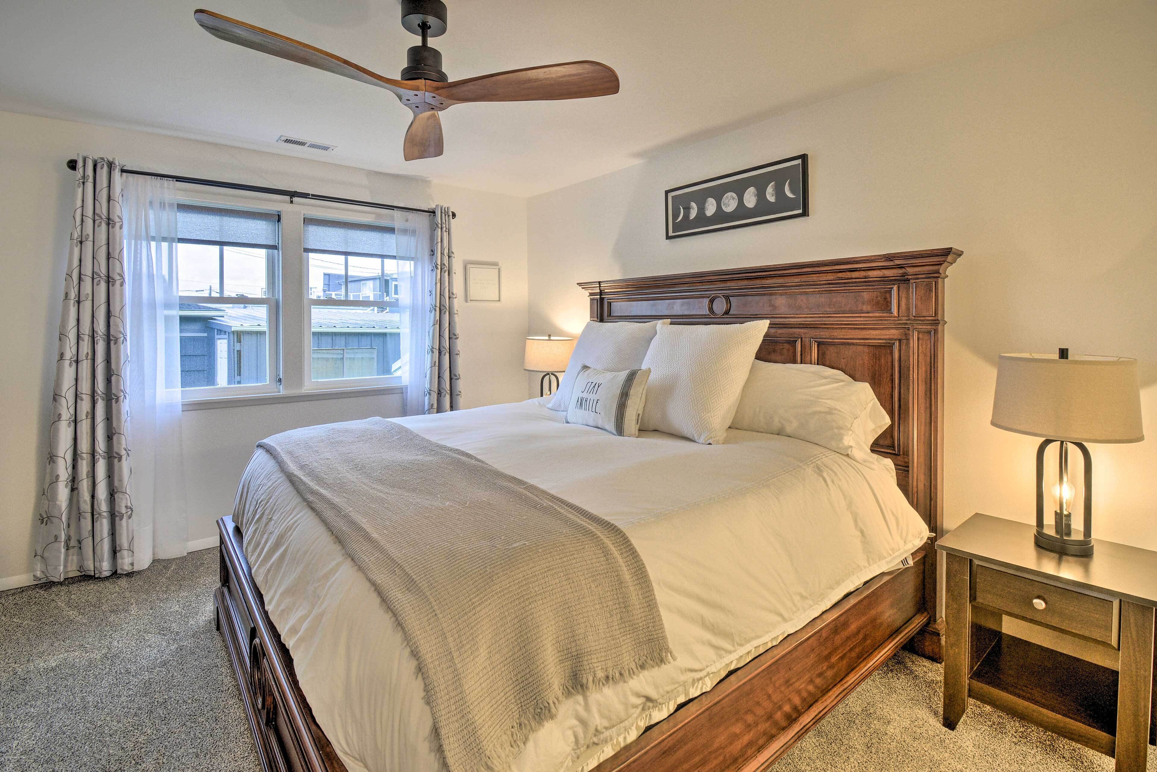 Un dormitorio con cama de madera, ventilador de techo, mesita de noche con lámpara y ventana con cortinas.