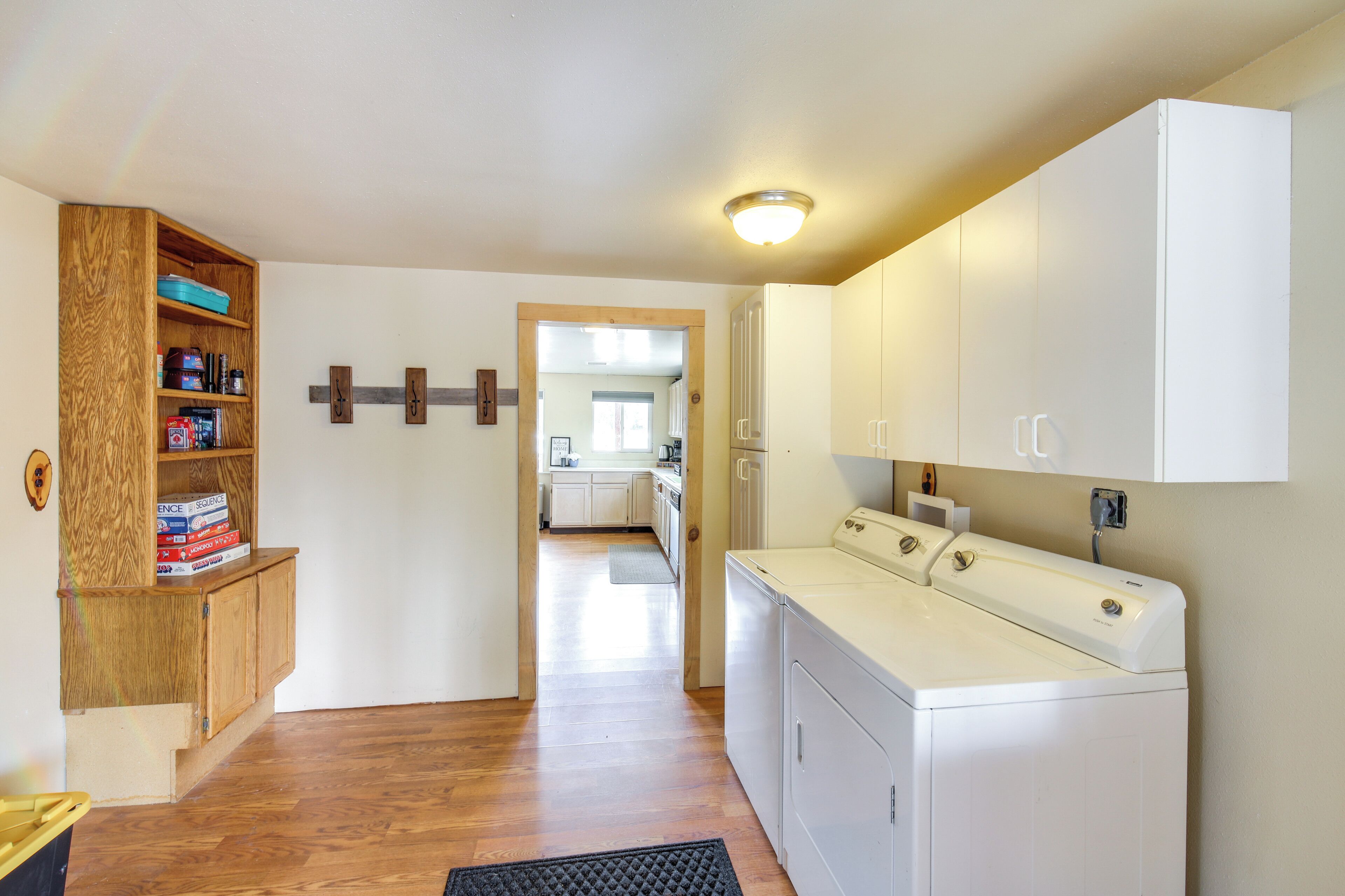 Une buanderie équipée d’un lave-linge, d’un meuble en bois avec des rangements et d’une porte donnant sur un espace cuisine.